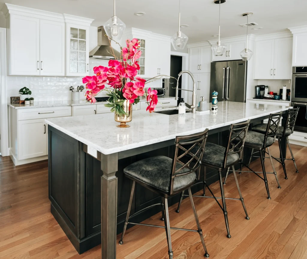 Layered kitchen design featuring contrasting cabinetry, upholstered barstools, natural wood flooring and vibrant floral accents.